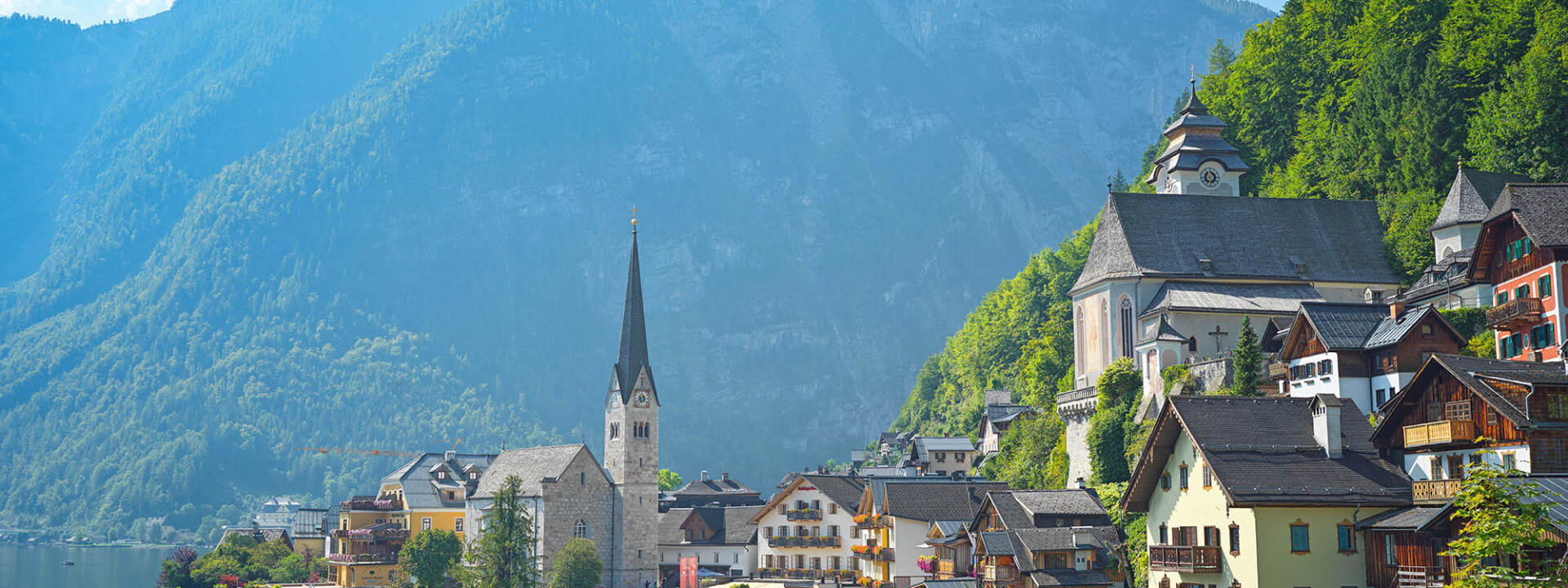 Hallstatt - Blick auf den Ort mit der Kirche, daneben der Hallstätter See und die Berge - Hallstatt Tour mit Salzburg Panorama Tours